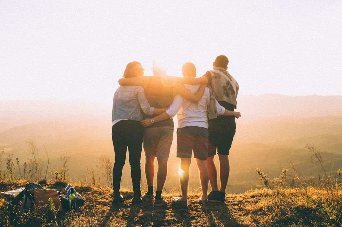 Friends standing arm in arm looking out over a valley at golden hour