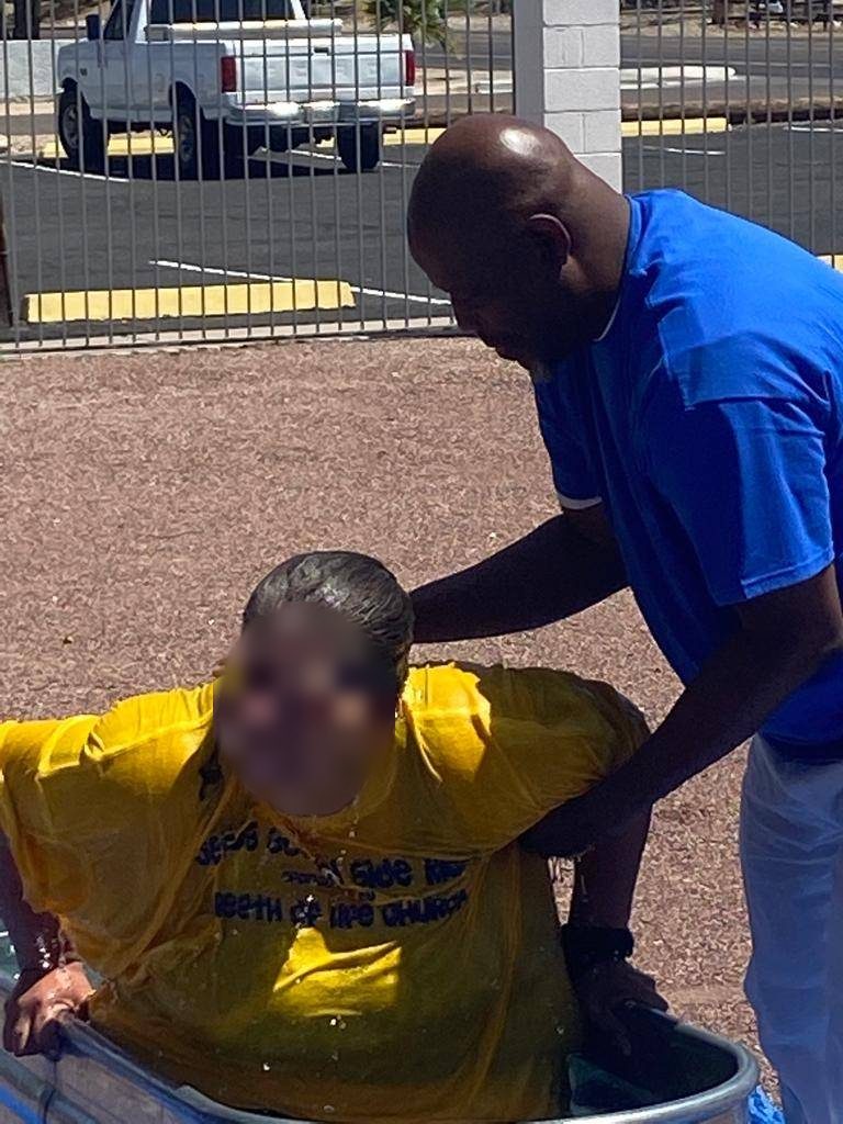 A person in a yellow shirt being baptized in an outdoor water trough