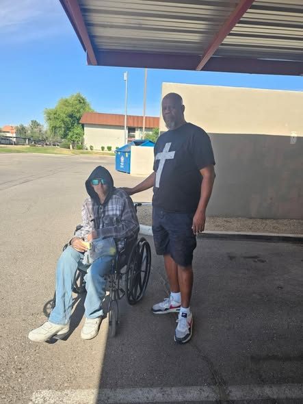 A volunteer standing beside a man in a wheelchair outside a building